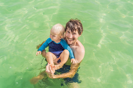 Father with his toddler son swimming in the turquoise waters of Lake Bacalar. Family bonding, summer...