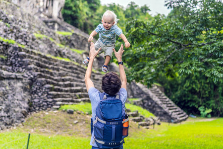 Father with his toddler son exploring the ancient pyramids of Palenque, Mexico, surrounded by dense jungle. Cultural heritage and adventure travel conceptの写真素材