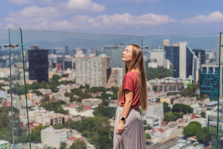 Female tourist or businesswoman standing on a skyscraper rooftop with a panoramic view of Mexico City. Travel or international business in Mexico conceptの写真素材