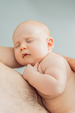 A baby peacefully falls asleep in his fathers arms, skin-to-skin. A heartwarming and intimate moment of love, bonding, and parenthood, showcasing the deep connection between father and childの写真素材