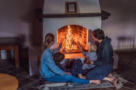 Family bonding by the fireplace during cozy winter evening. Warm and peaceful family moment indoors. Togetherness, love, and relaxation concept. A warm and inviting scene featuring a lit fireplace with glowing firewood. A colorful traditional rug and pillow lie on the floor, creating a cozy atmosphere. Home, relaxation, and rustic comfort conceptの写真素材