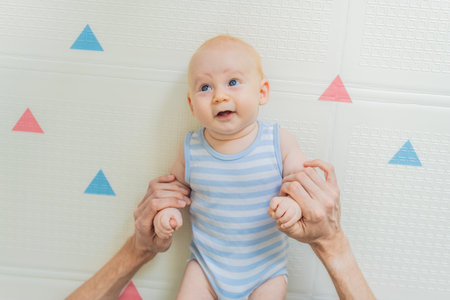 A baby lies on a soft children play mat while their father hands gently support and protect them. Heartwarming moment of care and connection. Parenthood, safety, and love conceptの写真素材