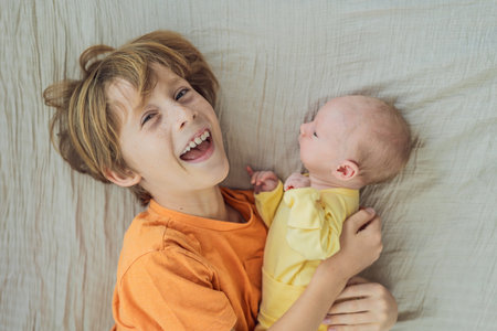 A young boy and his newborn brother lie together on a soft muslin blanket, sharing a tender sibling...