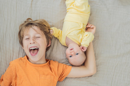A young boy and his newborn brother lie together on a soft muslin blanket, sharing a tender sibling moment. A heartwarming scene of brotherly love, bonding, and the beginning of a lifelong connectionの写真素材