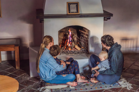 Family bonding by the fireplace during cozy winter evening. Warm and peaceful family moment indoors. Togetherness, love, and relaxation concept. A warm and inviting scene featuring a lit fireplace with glowing firewood and candles. A colorful traditional rug and pillow lie on the floor, creating a cozy atmosphere. Home, relaxation, and rustic comfort conceptの写真素材