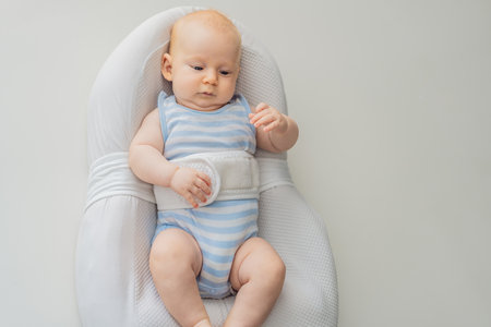 Adorable 3-month-old baby lying safely in a cozy infant cocoon secured with a special safety belt. Comfortable and protective design for newborn care. Parenting, safety, and baby comfort conceptの写真素材