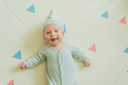 Adorable baby in a green hat lying on a play mat. Cozy newborn moment with soft textures and bright...