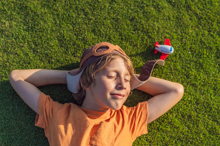 Boy wearing a pilot hat lying on the grass with a toy airplane, dreaming of adventures. Childhood, imagination, and freedom conceptの写真素材