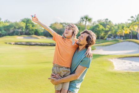 Father and son in the park, the boy wearing a pilot hat and holding a toy airplane, dreaming of adventures. Childhood, bonding, and imagination conceptの写真素材