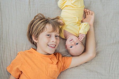 A young boy and his newborn brother lie together on a soft muslin blanket, sharing a tender sibling...