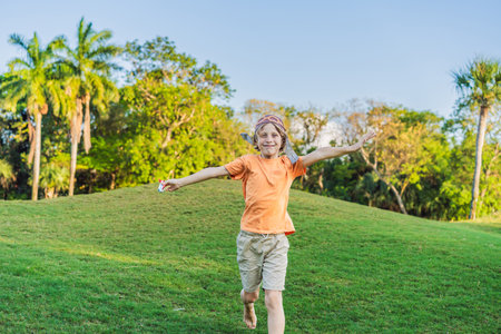 Boy wearing a pilot hat running through the grass with a toy airplane, dreaming of adventures. Childhood, imagination, and freedom conceptの写真素材