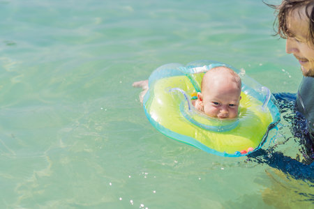 Father and newborn son swimming in the turquoise sea. Baby floating in an inflatable neck ring....