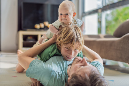 Father, son, and newborn baby lying on the floor in a cozy nursery, celebrating the arrival of their...
