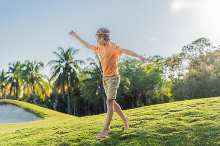Boy wearing a pilot hat running through the grass with a toy airplane, dreaming of adventures. Childhood, imagination, and freedom conceptの写真素材