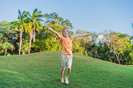 Boy wearing a pilot hat running through the grass with a toy airplane, dreaming of adventures. Childhood, imagination, and freedom conceptの写真素材
