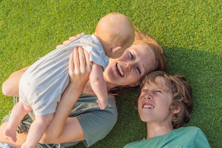 Mother, older son, and newborn baby on a meadow in the park. Family spending quality time together in nature. Parenthood, love, and family bond conceptの写真素材