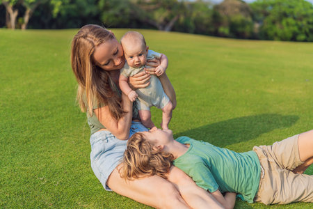 Mother, older son, and newborn baby on a meadow in the park. Family spending quality time together in nature. Parenthood, love, and family bond conceptの写真素材