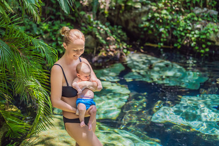 Mother with her baby standing by a Mexican cenote with turquoise water. Family adventure, travel, and nature bonding conceptの写真素材