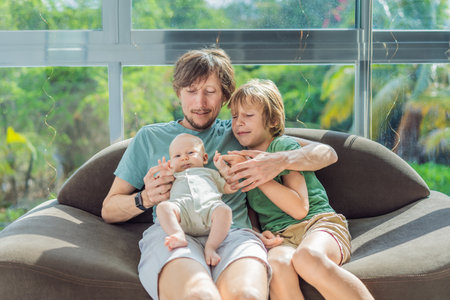 Father, son, and newborn baby sitting on the couch, joyfully celebrating the newest addition to...