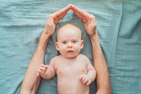 Father hands form a protective roof above baby head. Concept of safety, love, family protection, and...