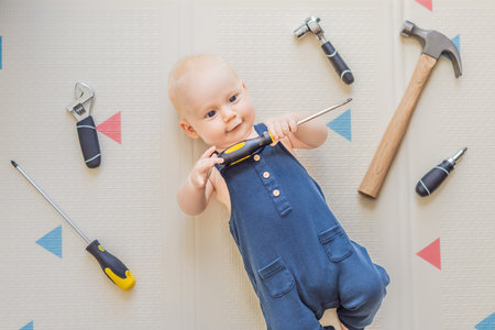 Adorable baby in a mechanic costume surrounded by toy tools. Concept of repair, imaginative play, and introducing kids to the world of fixing and problem-solving through funの写真素材