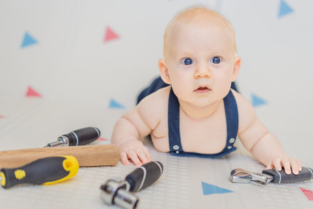 Adorable baby in a mechanic costume surrounded by toy tools. Concept of repair, imaginative play, and introducing kids to the world of fixing and problem-solving through funの写真素材