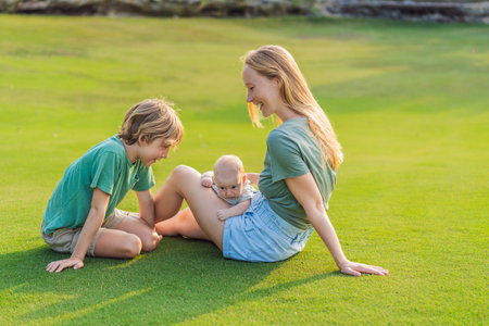 Mother, older son, and newborn baby on a meadow in the park. Family spending quality time together in nature.の写真素材