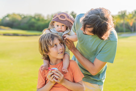 Father, son, and newborn on a meadow. Baby wearing a pilot hat, symbolizing dreams of aviation. Concept of family bonding, future pilot, and childhood aspirationsの写真素材