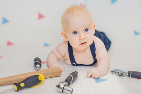 Adorable baby in a mechanic costume surrounded by toy tools. Concept of repair, imaginative play, and introducing kids to the world of fixing and problem-solving through funの写真素材