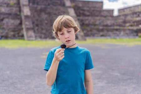 Boy tourist holding and observing a piece of obsidian in front of Teotihuacan pyramids, Mexico, symbolizing cultural discovery, archaeology, and educational travelの写真素材