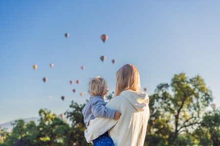 Mother with her young son as tourists, standing with colorful hot air balloons floating behind them over Teotihuacan, Mexico. Family travel, adventure, and cultural exploration conceptの写真素材