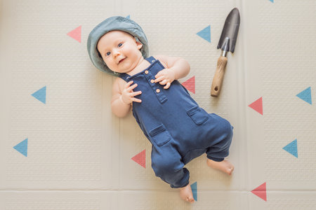 Adorable baby dressed as a little gardener with a small garden shovel nearby. Concept of gardening, nature connection, and playful early childhood imaginationの写真素材