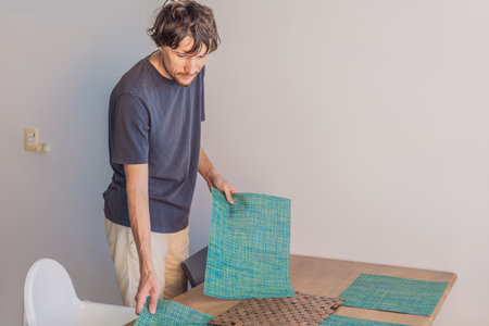 A man arranging placemats at a kitchen table in a bright modern home, captured in a candid moment...