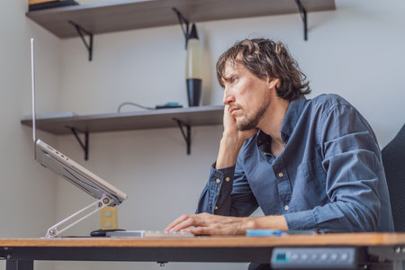 A man working from home in his organized home office, focused on his laptop in a bright modern workspace. Remote work, productivity, freelance lifestyle and contemporary global workplace conceptの写真素材