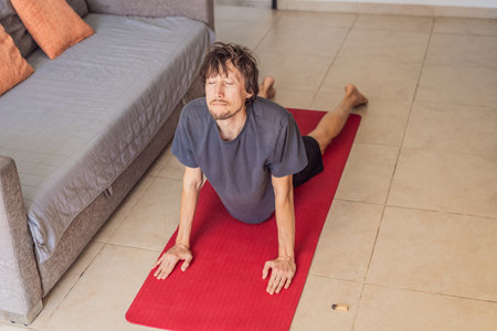 Man practicing yoga at home on a mat, performing calm stretching exercises in a cozy living room,...