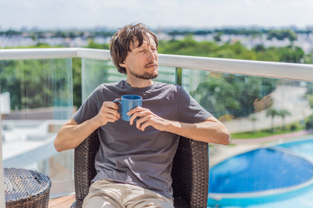 Man drinking coffee on the balcony in the morning. Concept of relaxation, lifestyle, routine, peaceful moments, and enjoying a warm drink outdoors at homeの写真素材