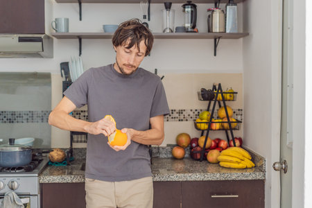 Man peeling a fresh orange in a bright kitchen, preparing a simple healthy snack. Concept of wellness, home cooking, daily routine, freshness, and natural food preparationの写真素材