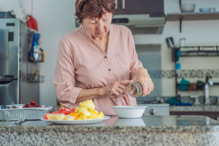 Elderly woman cooking in the kitchen, preparing a homemade meal with care and joy. Concept of healthy aging, independence, domestic life, culinary routine, and active senior lifestyle at homeの写真素材