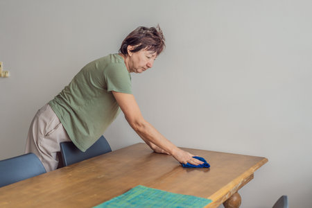 Unaltered senior woman cleaning and organizing a table at home, creating a tidy and comfortable...