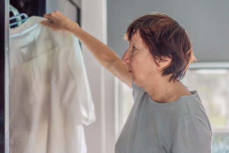 Elderly woman cleaning her home, organizing and tidying up with care in a bright living space. Concept of active aging, independence, daily routine, healthy lifestyle, and maintaining a comfortable home environmentの写真素材