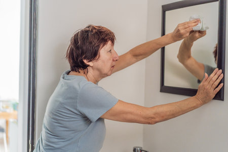 Elderly woman cleaning her home, organizing and tidying up with care in a bright living space. Concept of active aging, independence, daily routine, healthy lifestyle, and maintaining a comfortable home environmentの写真素材