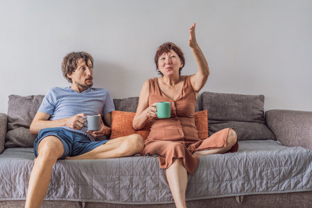 Older woman and her adult son relaxing together on the sofa while watching a comedy on television, enjoying a warm family moment at home. Entertainment, bonding and cozy lifestyle concept, representing comfort and togethernessの写真素材