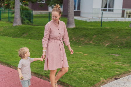 A mother walking with her young son in a sunny park, enjoying quality family time outdoors. Loving...
