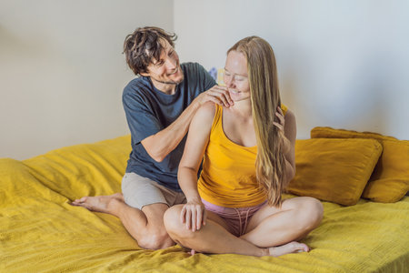 Man giving a gentle shoulder massage to a woman while sitting together on the bed, creating a warm and intimate moment at home. Relaxation, wellness, care and relationship concept, showing comfort, bonding and peaceful livingの写真素材