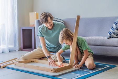 Father and his son assembling a table together in the living room at home. Meaningful family moment showing teamwork, learning and support. Fatherhood, home improvement and bonding through shared activity conceptの写真素材