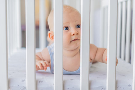 Sad baby looking through the bars of a crib, expressing longing and curiosity. Emotional scene...