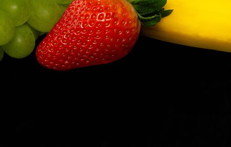 Strawberries, banana, grapes on a black background, place for text, assortment of exotic fruits isolated with copy space.の写真素材