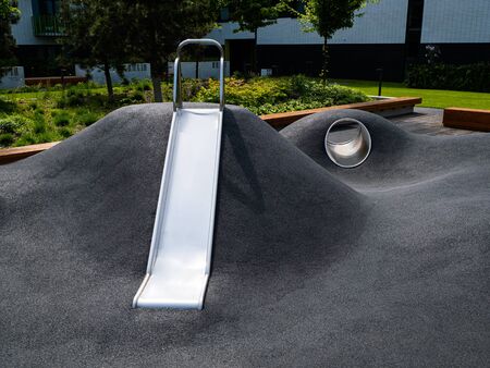 Modern playground with a metal slide inscribed in the landscape design. Gray playground without...