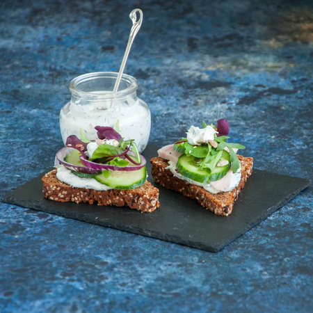 Rye seed crostini bread  with chicken ham  spring herbs red onion and spicy sour cream sauce served on a black stone board.の写真素材