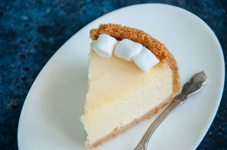 Slice of New York Cheesecake  style with marshmallows on white plate on blue backgroundの写真素材